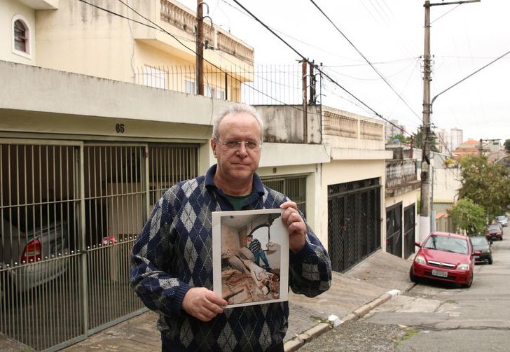 O jornalista Jorge Tadeu da Silva, um dos afetados pelo acidente com o avião modelo Fokker 100 da TAM que vitmou 99 pessoas em 1996, segura foto de como ficou a casa dele na rua Luís Orsini de Castro, no Jabaquara. - Foto: Rovena Rosa/Agência Brasil