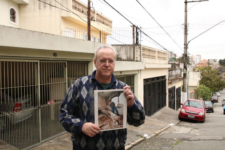 O jornalista Jorge Tadeu da Silva, um dos afetados pelo acidente com o avião modelo Fokker 100 da TAM que vitmou 99 pessoas em 1996, segura foto de como ficou a casa dele na rua Luís Orsini de Castro, no Jabaquara. - Foto: Rovena Rosa/Agência Brasil